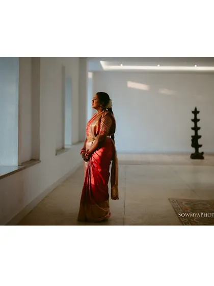 A full-length portrait of a bride in a red saree, bathed in the warm light of a setting sun. The minimalist space emphasizes her grace.