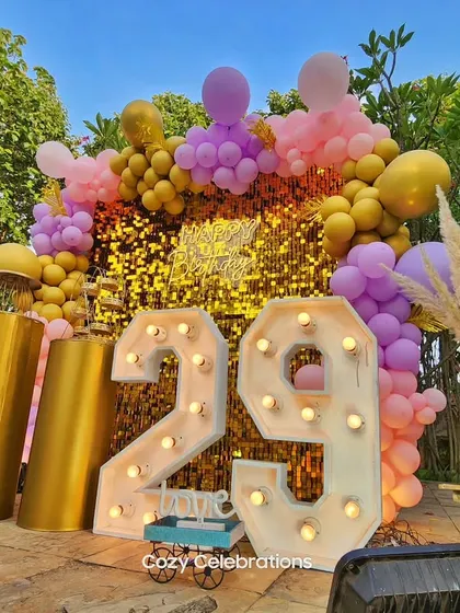 A vibrant and glamorous 29th birthday. The gold sequin wall is paired with gold, purple, and pink balloons and large marquee numbers for a fun, celebratory look.