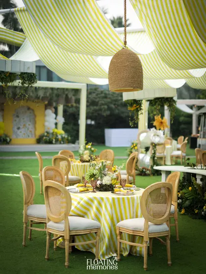 The elegant guest seating arrangement, with striped tablecloths and natural wood caned chairs, perfectly complements the sunny, garden-party vibe of this luxury baby shower.