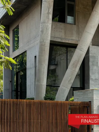 J-House, a finalist for The Plan Award 2024, seen from the exterior. The angled concrete columns and wooden fence create a distinctive and powerful architectural statement.