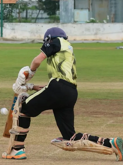 A batter plays a sweep shot during a competitive youth game.