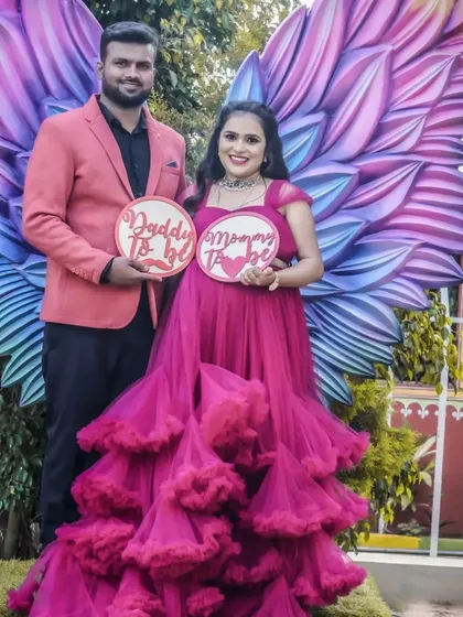 A duplicate of image 4, this photo shows a couple posing with "Daddy To be" and "Mommy To be" signs in front of a large, colorful angel wings prop, creating a fun and whimsical announcement.