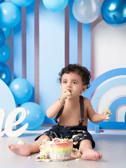 Getting messy during a first birthday cake smash! The blue-themed setup is perfect for this little boy's celebration, and the rainbow cake adds a pop of color.