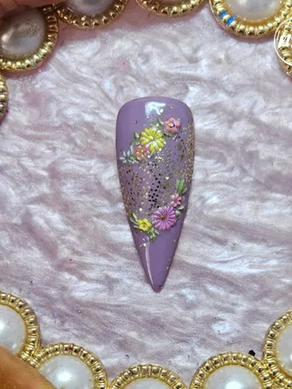 A single, beautiful nail showcasing a student's hand-painting skills. The tiny, detailed flowers on a purple glitter base are just gorgeous.
