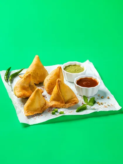 Crispy samosas with chutneys, shot against a vibrant green screen for Bistro by Blinkit. This style is perfect for e-commerce platforms and apps, allowing for easy background removal and consistent branding.