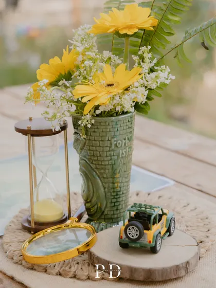 A close-up of the safari-themed table centerpiece, featuring a miniature jeep, an hourglass, and yellow gerberas. These small, thematic details bring the entire concept to life.