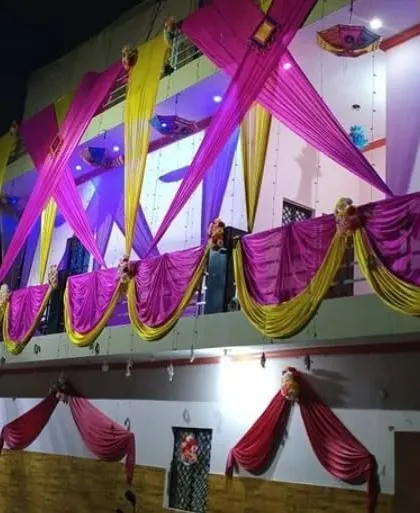 A house facade decorated at night with pink and yellow drapes in a criss-cross pattern, illuminated by blue and purple lights.