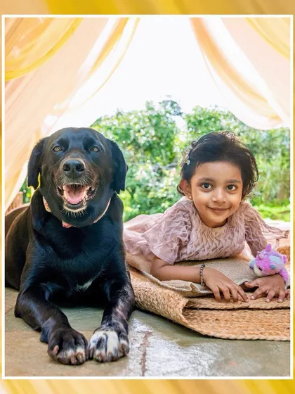 A beautiful portrait of a little girl and her happy black lab sitting together under a yellow canopy.