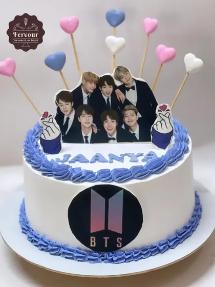 A classic BTS theme cake for a true fan. The cake is decorated with the band's logo, an edible photo of the members, and heart-shaped lollipops, all in the signature purple and white colors.