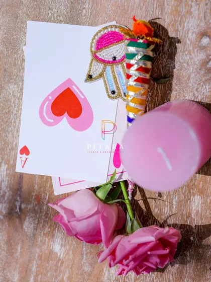 A flat lay of some of the custom stationery and favors, including a playful playing card and a beaded brooch, all tied into the event's color scheme and theme.