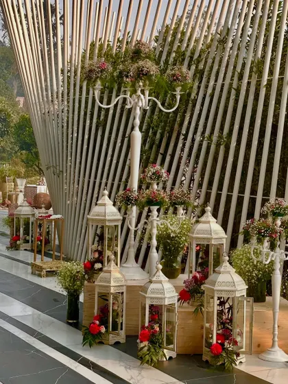 White candelabras and lanterns filled with flowers, set against a modern white slatted backdrop.