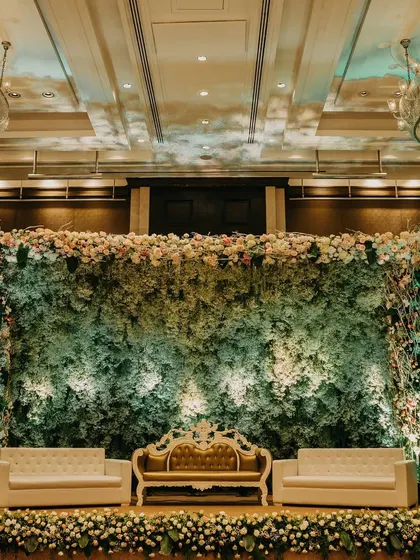 A stunning reception stage where a wall of delicate gypsophila creates a cloud-like effect. The design is framed with pastel florals and features elegant seating for a sophisticated look.