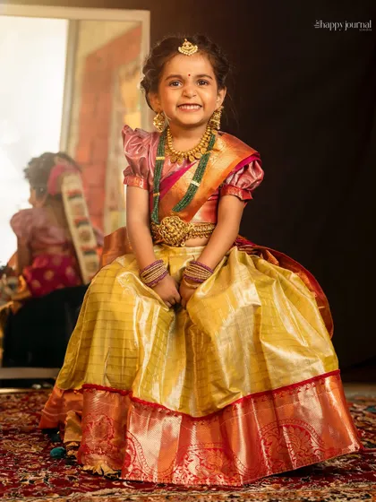 A girl in a traditional silk lehenga smiles brightly, her reflection visible in the mirror behind her. A joyful celebration of culture.