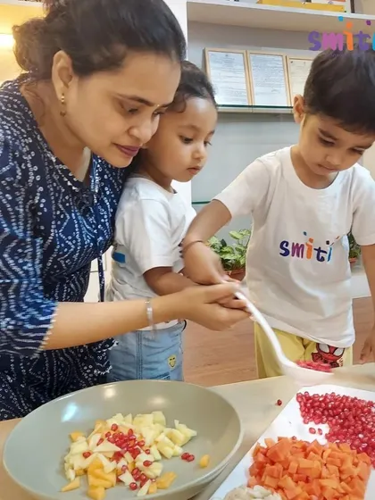 A teacher guides two toddlers as they mix a colorful fruit salad. This shared activity is a wonderful way to practice social skills like taking turns and helping one another.