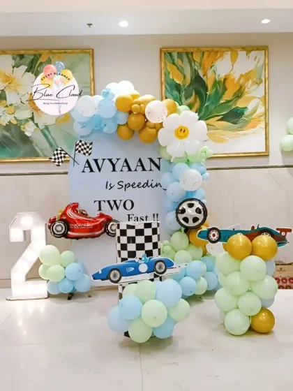 A creative "speeding two fast" race car theme for a second birthday. This decoration features a custom backdrop, balloon arrangements in theme colors, car cutouts, and a large marquee number '2'.