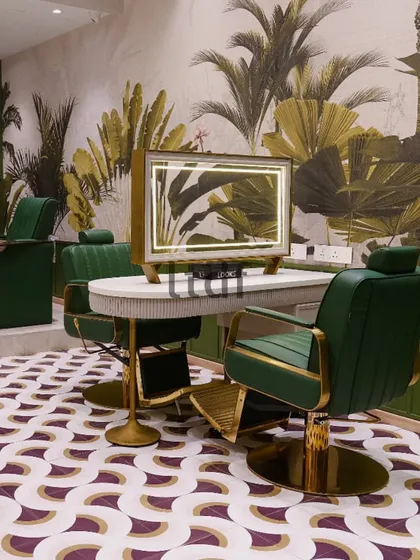 A close-up of the styling station at Looks Salon, where the custom-designed mirror with integrated lighting sits atop a fluted white counter. The rich green leather and brushed gold accents of the chair add a layer of opulence.