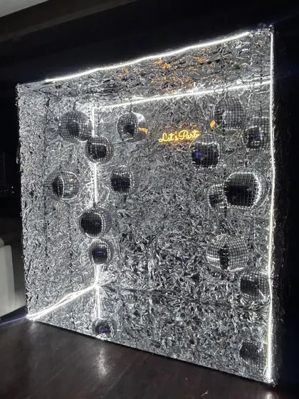 A unique 3D photo op. This silver shimmer cube is lit with neon strips and filled with disco balls, creating a futuristic and immersive space for guests to take pictures.