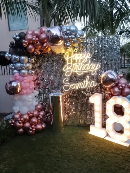 An outdoor 18th birthday party setup on the grass, with a sequin wall, personalized neon sign, and marquee numbers.