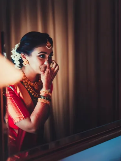 A reflection shot of the bride applying her bindi, adding a layer of artistry to the documentation of her preparation.