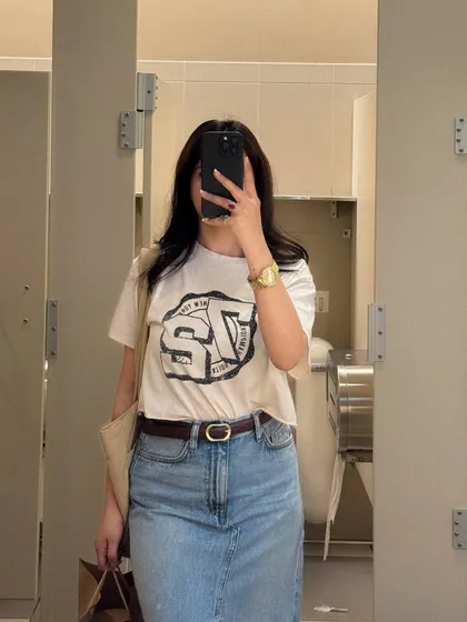 A mirror selfie showing off a casual OOTD with a graphic tee and long denim skirt.