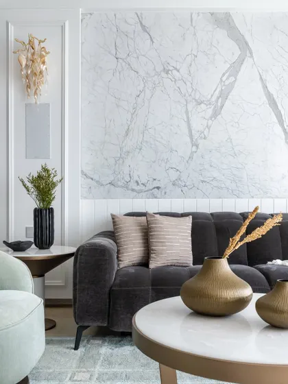 A detail shot of the living room's decor, showing the combination of a tufted charcoal sofa, a marble-topped coffee table, and elegant wall sconces.