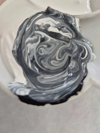 A satisfying swirl of black and white acrylic paint on a palette, ready for a new creation.