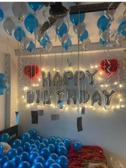 A simple birthday room surprise with blue balloons on the floor, "Happy Birthday" foil letters, and fairy lights.