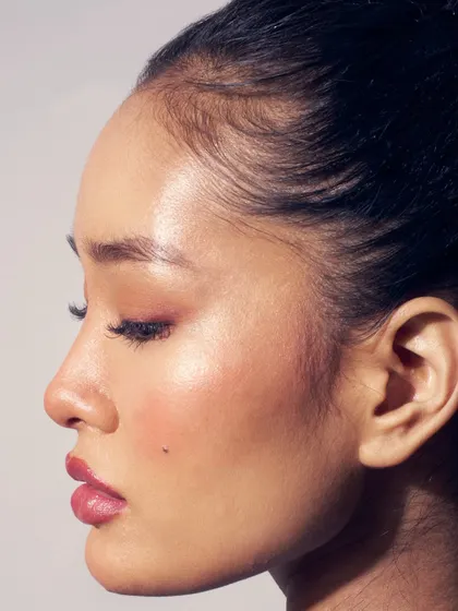 A profile shot highlighting a 'glass skin' finish. The skin is incredibly dewy and reflective, with a soft touch of pink on the eyes and cheeks.