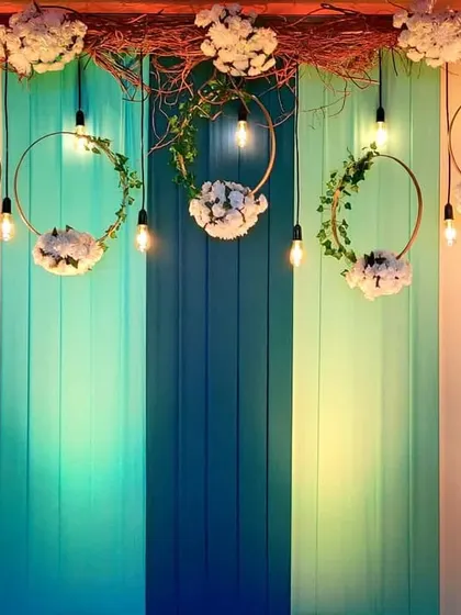 A close-up of the rustic and colorful photo backdrop for the Mehendi. We combined a painted wood panel with hanging floral wreaths and Edison bulbs for a unique and stylish look.