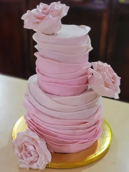 A stunning two-tier wedding cake with an ombre pink ruffle effect. The delicate, flowing texture was created entirely with buttercream, accented with handmade sugar roses.