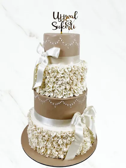 Another one of our stunning multi-tiered wedding cakes. This four-tier cake is adorned with delicate ruffles, satin bows, and intricate pearl detailing for a classic, romantic look.