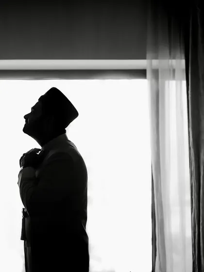 A powerful silhouette of the groom. This black and white shot, taken against a bright window, captures a quiet, contemplative moment before the ceremony.
