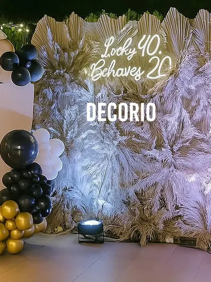 This premium birthday backdrop uses a wall of dried pampas grass for a unique, textural look. A custom neon sign and a black, white, and gold balloon arrangement add a touch of modern elegance.