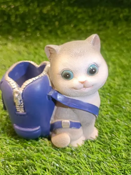 A sweet grey cat pen holder with a blue backpack. It's a whimsical and practical item for anyone who loves feline friends.