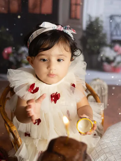 A close up of the birthday girl, with the single candle on her cake in focus. This shot beautifully captures the magic of a first birthday wish.