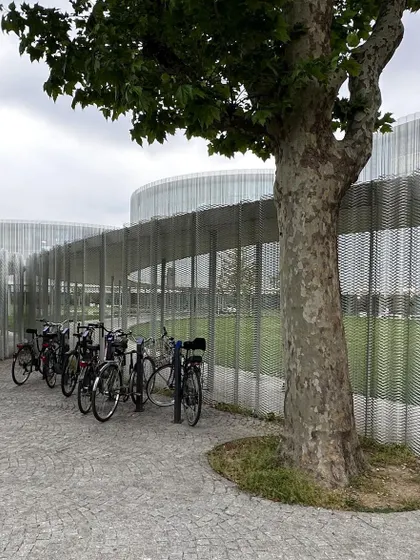 Bicycles parked against the translucent metal mesh facade. This simple, everyday scene highlights how even the most high design architecture must accommodate the mundane realities of daily life.