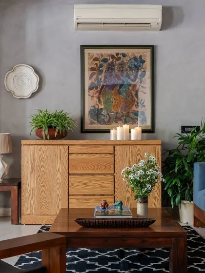 A detail of the lounge area, focusing on the curated decor. A wooden credenza holds candles, plants, and a gallery wall of art, adding layers of personality to the eclectic, modern Indian space.