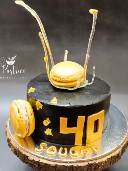A sleek and modern cake for a 40th birthday, featuring a black finish, gold accents, and a caramel macaron with a sugar splash.