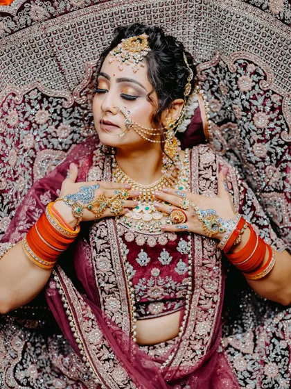 A full-body shot of the bride lying down, showcasing the magnificent spread of her heavily embroidered velvet lehenga. An artistic and grand portrait.