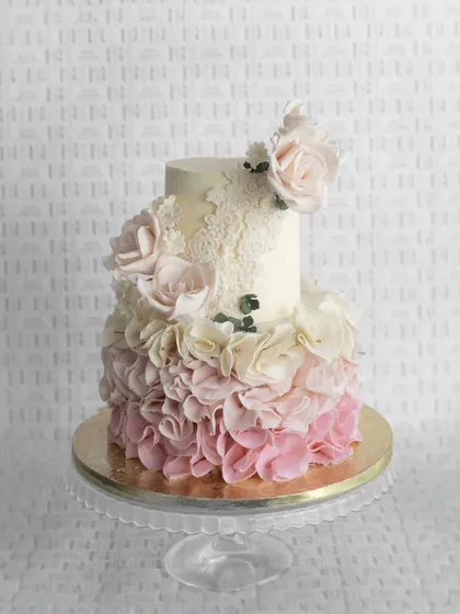 A two-tiered wedding cake with a beautiful gradient of pink ruffles. This design is perfect for a romantic and whimsical celebration, topped with fresh roses and delicate lace details.