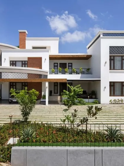 A daytime view of a modern villa, showcasing how the structure interacts with the surrounding landscape. The clean white walls are accented with wood and stone, creating a connection to nature.