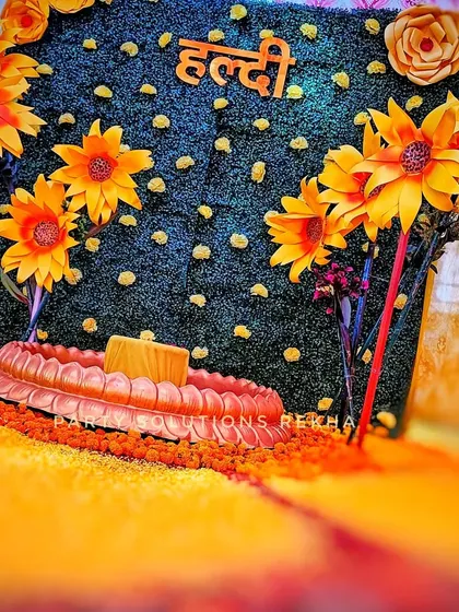 A vibrant Haldi setup featuring a sunflower theme. The faux grass backdrop with the 'Haldi' sign and a floor of marigold petals creates a bright and cheerful atmosphere.