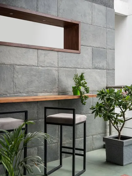 This outdoor bar area is a perfect example of bringing the indoors out. The slate stone wall continues from the living room, creating continuity, while the simple black bar stools and potted plants make it a chic, green escape.