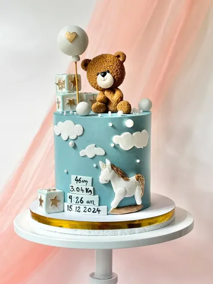 A beautiful birth announcement cake in a lovely shade of blue. It features a custom block with the baby's birth stats, a teddy bear, and a rocking horse.