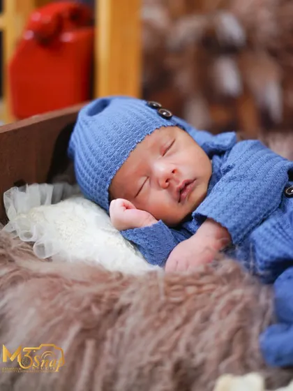 A close-up of a sleeping newborn in a cozy blue outfit. The soft textures and peaceful expression make this a classic and timeless shot.