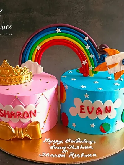 A beautiful cake for twins, with a pink princess theme for her and a blue space rocket theme for him, united under a rainbow.