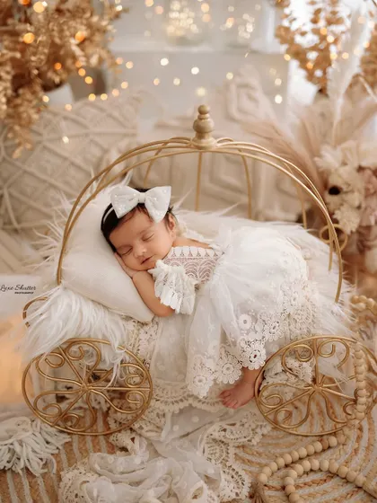 Our newborn sessions are designed to be a work of fine art. Here, a 15-day-old princess sleeps peacefully in a boho-themed carriage prop, surrounded by soft textures and warm light, showcasing our attention to detail in creating a dreamy, serene atmosphere.