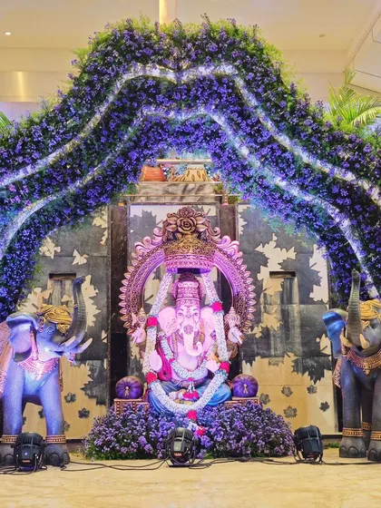 A majestic Ganesha installation for a wedding ceremony. The deity is framed by a grand arch of purple flowers and flanked by two decorated elephant statues, creating a powerful spiritual centerpiece.