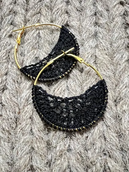 My black crochet hoop earrings on a textured background. They are a perfect mix of modern style and handmade craft.
