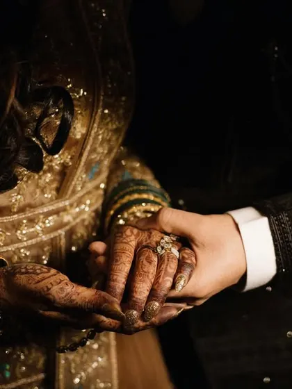 A close-up shot focusing on the couple's intertwined hands. This detailed image symbolizes their union and commitment, capturing the texture of their ornate outfits and the bride's henna.